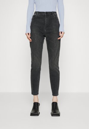 Jeans de cintura alta, cinza escuro, com um corte ajustado, costuras contrastantes e uma textura desbotada, combinados com mules pretos de bico aberto.