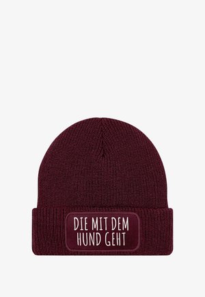 Maroon knit beanie with a ribbed texture and a folded cuff. Features a rectangular patch with white text: "DIE MIT DEM HUND GEHT."