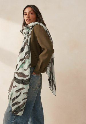 Lightweight, patterned scarf featuring shades of green and brown, with a textured design and fringed edges, draped elegantly.