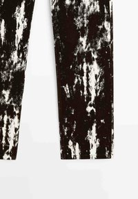 Leggings avec un motif abstrait éclaboussure de peinture noir et blanc et coupe droite, présenté sur un fond blanc.