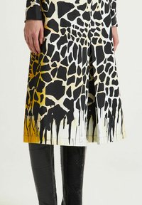 Abito con stampa giraffa in tessuto nero, crema e giallo, caratterizzato da un taglio dritto e orlo drappeggiato, abbinato a stivali in pelle nera lucida.