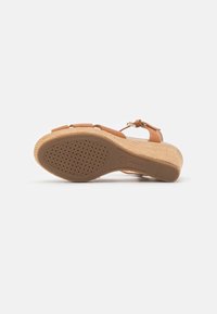 Sandale beige avec un talon en liège texturé, dotée de sangles ajustables et d'une semelle en caoutchouc durable avec des perforations pour une meilleure traction.