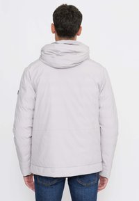 Giacca con cappuccio grigio chiaro dalla texture liscia, polsini elastici e vita elasticizzata. Presenta cuciture laterali e dettagli di cucitura sottili.