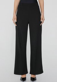 Pantalones negros de pierna ancha hechos de una tela suave con una cintura plana y sin bolsillos visibles. Presentan una silueta limpia y estilizada.