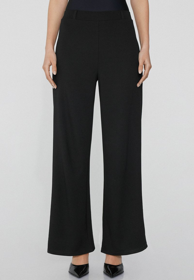 Pantalones negros de pierna ancha hechos de una tela suave con una cintura plana y sin bolsillos visibles. Presentan una silueta limpia y estilizada.