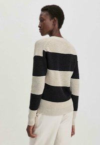 Strickpullover mit horizontalen Streifen in Creme und Schwarz. Strukturierter Stoff mit gerippten Bündchen und Saum, der eine lockere Passform zeigt.