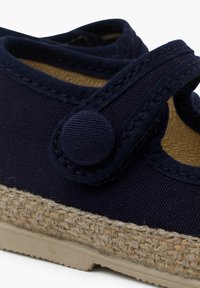 Zapatos de lona en color navy con suela de yute trenzado, que presentan un botón redondo y una correa de velcro para un ajuste ajustable. Detalle de tela texturizada.