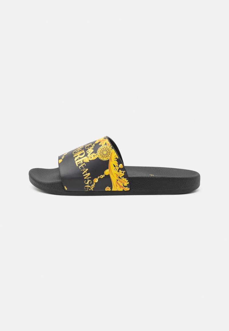 Sandale à enfiler noire avec motif baroque jaune et design chaîne dorée sur la bride, semelle noire unie, vue de côté.