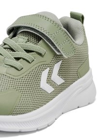 Grøn atletiksko med mesh, forstærket tå, polstret krave, hvide detaljer og en velcrolukning. Gummisål med struktureret mønster.