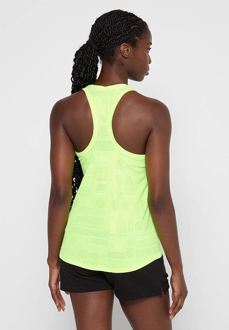 Helles limegrünes Tanktop mit Racerback-Design und Netzstruktur, ausgestattet mit gemusterten Ausschnitten. Kombiniert mit schwarzen Shorts.