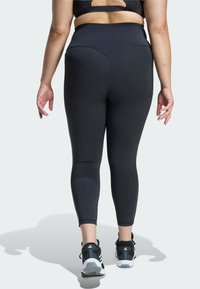 Black high-waisted leggings with a fitted design and smooth texture, featuring a seam detail at the back and complemented by black athletic shoes.
