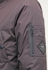 Dark gray jacket sleeve with a zippered pocket and a Vans logo patch reading "Original Vans Off The Wall Since 1966."