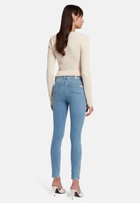 Jeans aderenti azzurri con una texture liscia, vita alta e tasche posteriori. Abbinati a un maglione strutturato di color crema e mules con tacco.