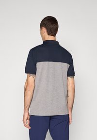 Polo-skjorte med marineblå øvre seksjon og grå nedre seksjon, kortermet, glatt tekstur og klassisk krage-design.
