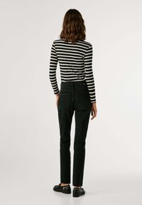 Melnas taisnās kājas džinses ar augstu jostasvietu, papildinātas ar melnu un baltu svītrainu ilgām piedurknēm. Redzamas aizmugurējās kabatas un minimāls aparatūras daudzums.