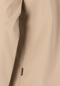 Beige lichtgewicht jack met een gladde textuur, voorzien van een ritszak en een klein zwart label nabij de naad.