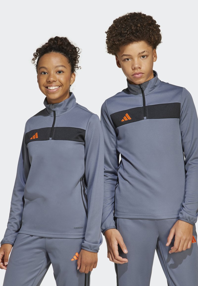Sudaderas deportivas grises con cremallera, con una franja horizontal negra y acentos de logo naranja, combinadas con pantalones grises a juego. Tejido suave y transpirable.