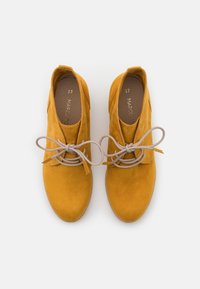 Stivali alla caviglia in suede giallo con punta arrotondata, caratterizzati da un design con lacci beige e una texture morbida. Taglia 37 visibile all'interno.