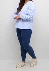 Lichtblauw, gestreept, blouse met lange mouwen, een V-hals en pofmouwen, gecombineerd met donkerblauwe skinny jeans en beige sneakers.