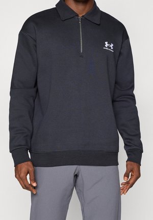 Sort langærmet sweatshirt med kvart lynlås og Under Armour-logo på venstre bryst, båret med grå bukser, vist fra skuldre til hofter.