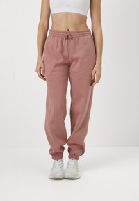 Joggers in cotone rosa chiaro, con vita elasticizzata e polsini. Presentano un dettaglio con coulisse e una vestibilità comoda. Indossati con sneakers bianche.