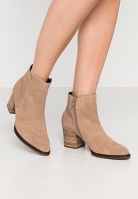 Beżowe zamszowe botki za kostkę z ostrym noskiem i bocznym zamkiem, z teksturowanym, warstwowym obcasem dla lepszej stabilności.