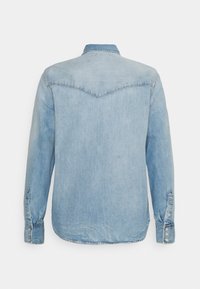 Camicia in denim azzurro chiaro con maniche lunghe, colletto a punta e chiusura con bottoni sui polsini, con cuciture a vista e dettaglio della sella sul retro.