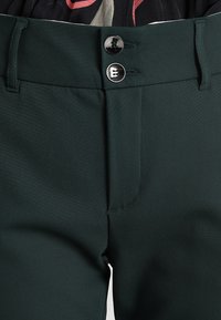 Mörkgröna byxor med en mjuk textur, som har två silvriga knappar i midjan och en klassisk skräddarsydd design med bältesöglor.