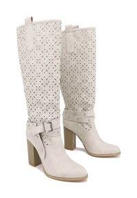 Stivali finti in pelle bianca, alti fino al ginocchio, perforati, con un tacco spesso, cinturino regolabile con fibbia e dettagli in chiodo attorno alla caviglia.