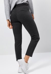 Pantalons ajustés gris foncé, avec une texture lisse, arrivant aux chevilles, dotés d'une ceinture à rayures noires et grises et de poches arrière. Associés à des baskets blanches.