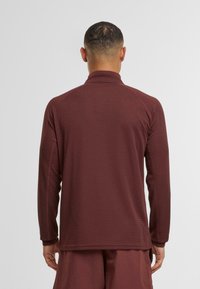 Bordeaux-rotes Langarm-Oberteil mit hohem Kragen, strukturiertem Stoff und taillierten Schnitt. Verfügt über dezente Nähte und einen geraden Saum.