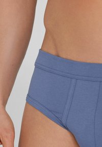 Světle modré bavlněné spodky s hladkou texturou, vybavené širokým elastickým pasem a dvojitým stehem na bocích.