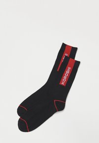 Calcetines negros con acentos rojos, que presentan un diseño de logo y rayas. Están hechos de un material elástico y tienen una textura suave.