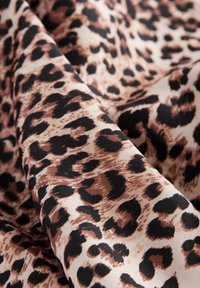 Tessuto con stampa leopardata caratterizzato da una combinazione di macchie nere su uno sfondo crema, che mostra una texture liscia e una qualità di drappeggio morbida.