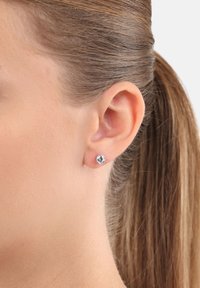 Sterling silver stud earrings with round clear crystal, featuring a polished finish and a secure post back, displayed beside a model's ear.