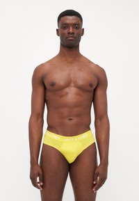 Žlté pánske slipy s bielym elastickým pásom, s názvom značky "JACK & JONES" napísaným veľkými písmenami. Hladká textúra a priliehavý dizajn.