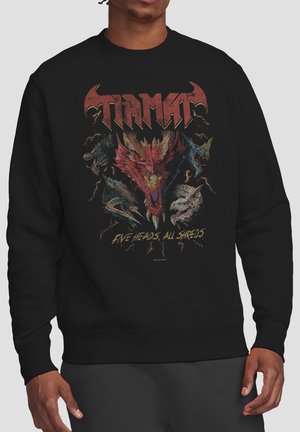 Person wearing black sweatshirt with five detailed dragon heads and text "Tiamat" and "Five Heads, All Shreds" on the front.