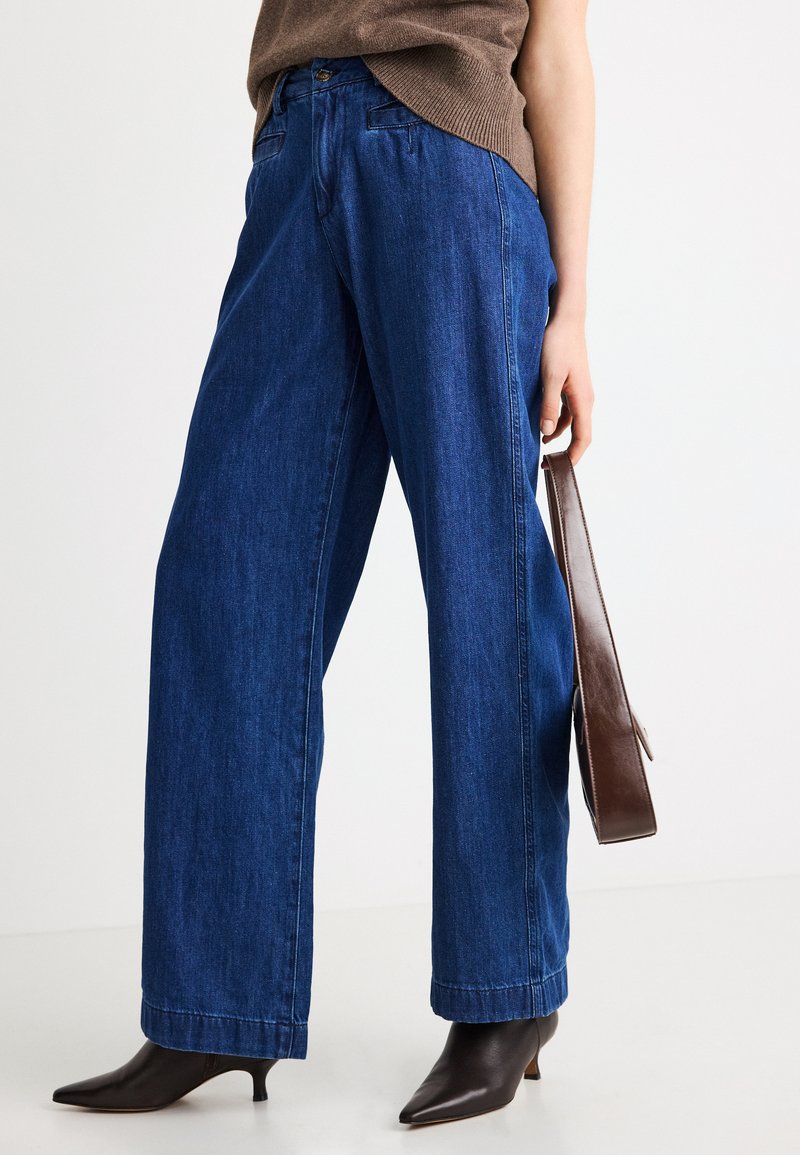 Φαρδιά μπλε τζιν παντελόνια με ψηλή μέση, διαθέτουν κλασικό σχέδιο με πέντε τσέπες και εμφανές σκούρο ράψιμο κατά μήκος των ραφών.