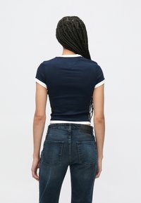 Tmavomodré priliehavé tričko s krátkym rukávom a bielym lemovaním, skombinované s vysokým pásom tmavomodrých džínsov. Hladká textúra a štíhly strih.