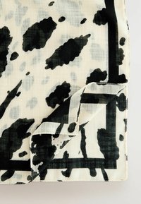 Tissu léger avec un motif animal en noir et blanc présentant des taches irrégulières. Les bords sont ourlés, et une bordure noire met en valeur le design.