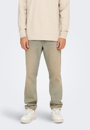 Lys grøn denimjeans og en beige langærmet skjorte, parret med hvide sneakers. Jeansene har en afslappet pasform og let falmning.