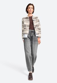 Giacca cropped multicolore e texture con colletto bianco, abbinata a jeans grigi a vita alta e zoccoli scuri con borchie argentate.