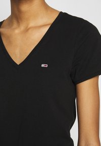 Černé bavlněné tričko s výstřihem do V, na levé části hrudi je malé vyšívané logo v červené, bílé a modré barvě. Krátké rukávy.