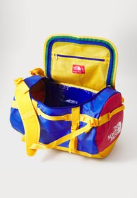 Multicolored duffle bag with a blue body, yellow straps, and red accents. Features a zippered top, mesh pocket, and branded label inside.