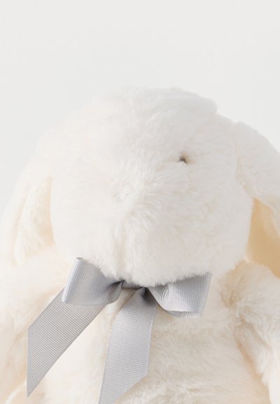 Μαλακό λευκό παιχνίδι αρνάκι με πεσμένα αυτιά και λαμπερή ασημί κορδέλα δεμένη σε φιόγκο γύρω από το λαιμό του, σε λευκό φόντο.