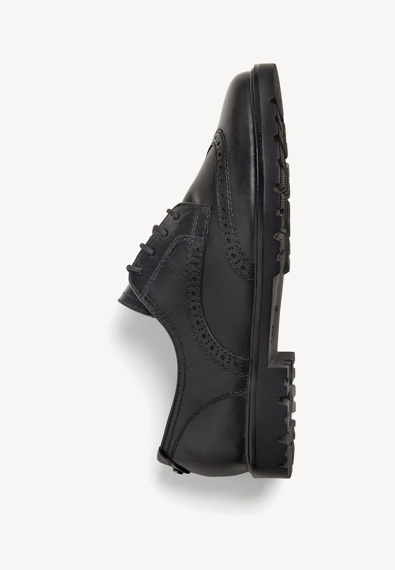 Chaussure noire en cuir avec un design brogue, des côtés texturés et une semelle en caoutchouc épaisse. Présente des lacets visibles et des perforations décoratives.