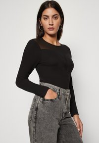 Top negru cu maneci lungi, cu un panou transparent la umeri, purtat cu blugi gri din denim cu talie înaltă. Mici embellishments, design fit.