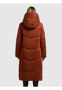 Abrigo largo acolchado en color óxido con capucha. Presenta costuras en forma de chevron, textura suave y un pequeño logo en la parte inferior izquierda.
