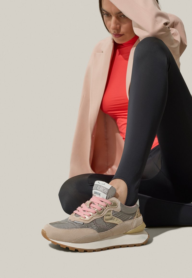 Grå och beige sportiga sneakers med rosa snören, textilmaterial och guldiga detaljer. Vit sula med ljusbrunt mönster.