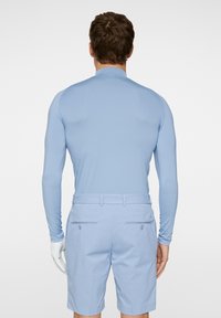 Vaaleansininen pitkähihaisten paita, jossa on sileä pinta, yhdistettynä vaaleansinisiin kuviollisiin shortseihin, joissa on takataskut ja vyölenkit.